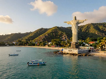 Cristo Rei statue overlooking turquoise Dili Bay with fishing boats and tropical hills, iconic East Timor landmark for dating couples