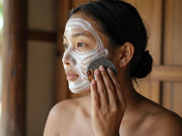 Burmese woman applying traditional thanaka cosmetic paste in circular patterns on cheeks, representing authentic Myanmar beauty traditions in dating