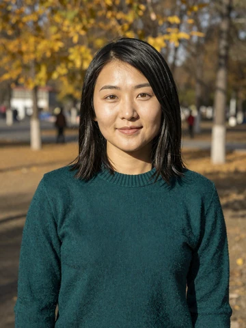 Mongolian woman in teal sweater smiling in autumn park in Ulaanbaatar, representing genuine Mongolian dating profiles