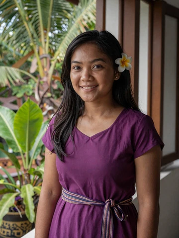 Timorese woman in plum dress with tais belt and flower in hair near window, representing modern Timorese singles on iDatingZone