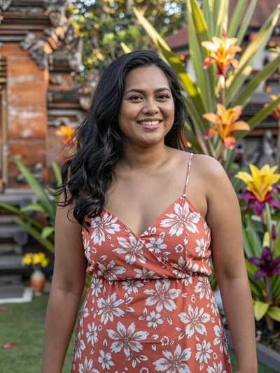 Dewi, 29, Indonesian woman from Bali near temple garden in coral sundress