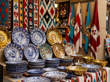 Traditional Uzbek ceramics and ikat textiles at Bukhara bazaar with vibrant blues and golds, showcasing rich Silk Road cultural heritage